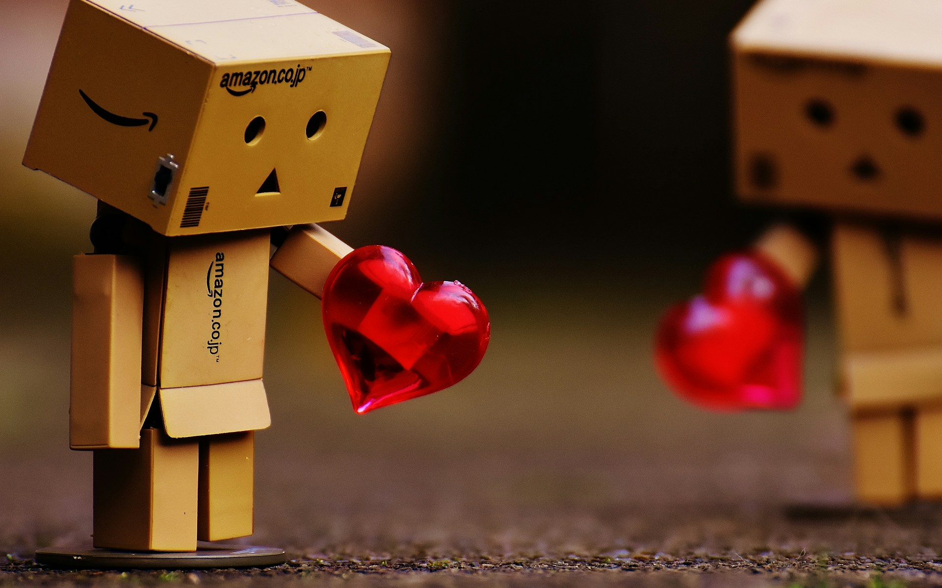 Danbo figure - a small robot made from Amazon packaging - offers a translucent red heart to another cardboard figure already receding out of focus