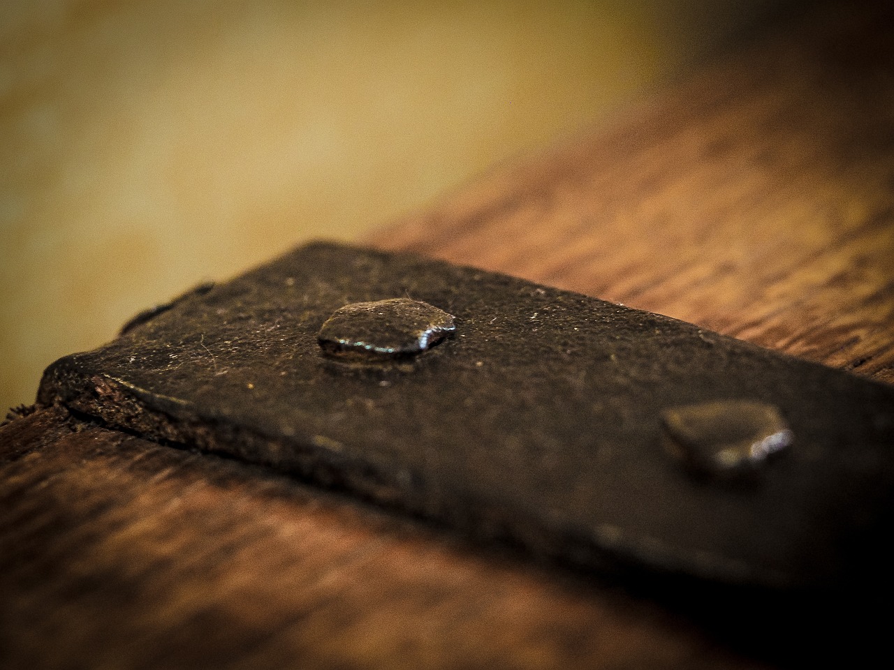 A worn iron bracket fixed with a rivet to a piece of dark, aged wood, lit warmly in close-up.
